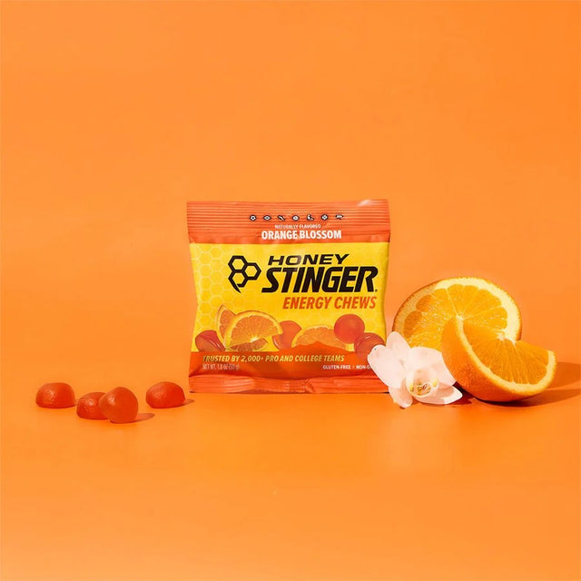 Honey Stinger energy chews package with orange slices and flowers on an orange background