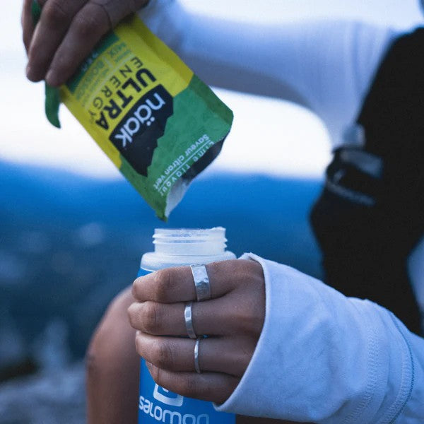 Pouring a single serve packet of naak energy drink mix into a soft flask