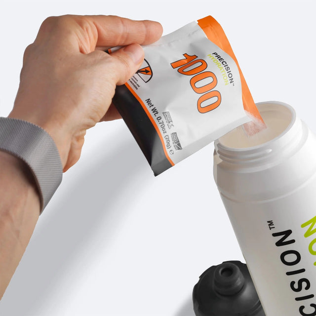 Hand pouring a packet of Precision Hydration 1000 electrolyte mix into a water bottle