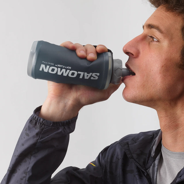Person drinking from a blue Salomon soft flask with hand strap