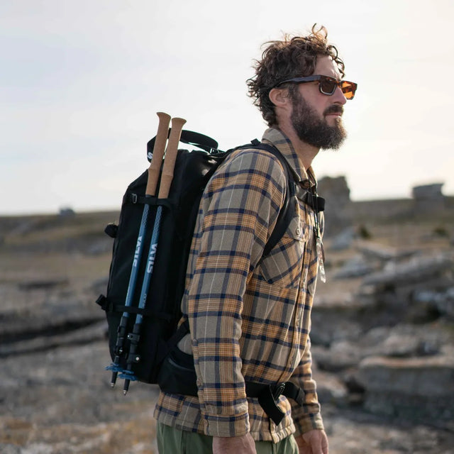 Man with a backpack and hiking poles attached walking on a rocky landscape