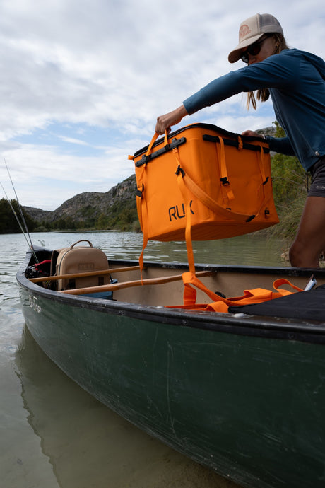 Person loading an orange RUX gear box into a canoe