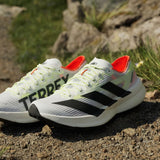 Adidas Terrex running shoes with black stripes and orange accents on a rocky surface.