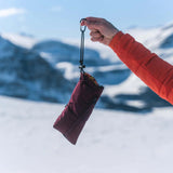 Person holding a maroon phone warmer pouch with a carabiner against a snowy mountain backdrop