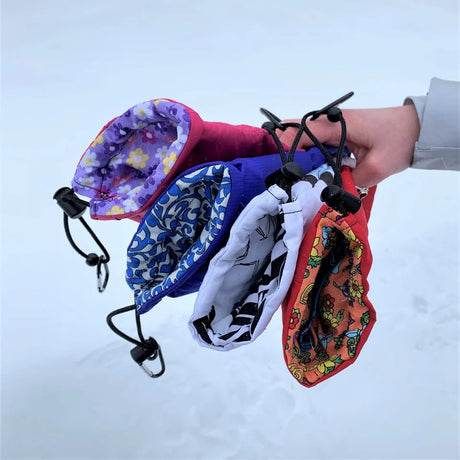 Colorful drawstring phone bags with various patterns held by a hand against a snowy background