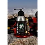 A pump bottle of climbon lotion crème  displayed on a red carabiner on a rock with climbing gear and a mountain background