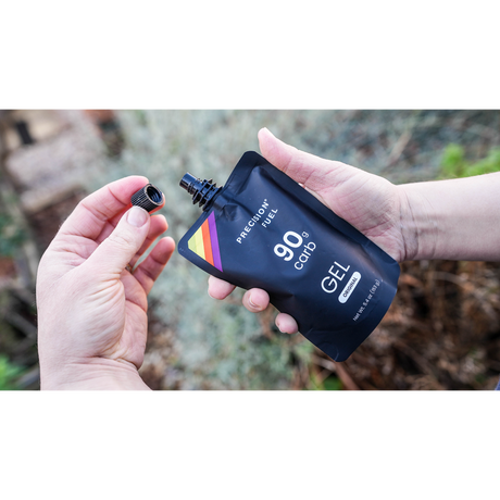 Person holding a Precision Fuel 90 gel container outdoors.
