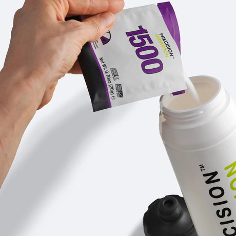 Hand pouring a packet of Precision Hydration 1500 electrolyte mix into a water bottle