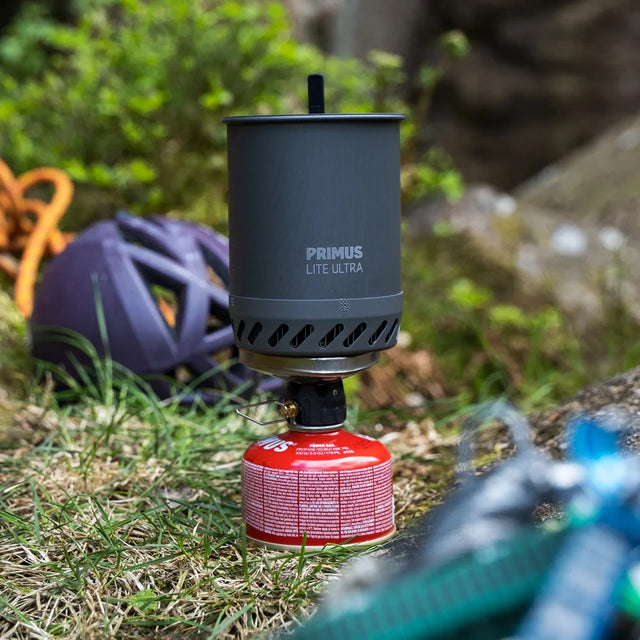 Primus Lite Ultra stove on a grassy outdoor setting with a helmet and backpack in the background.