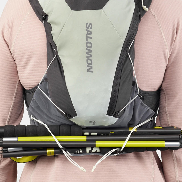 Back on-model view of green/grey Salomon ADV Skin 12 running vest with hiking poles attached