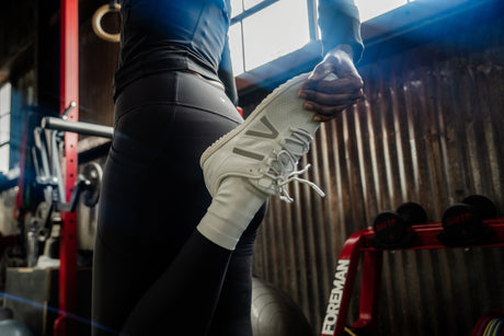 Person wearing white sneakers doing a quad stretch in a gym setting