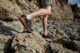 Person wearing black shoes with orange soles on a rocky surface